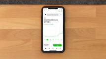 Stock trading app on smartphone displaying Robinhood Markets price on wooden desk. (Foto: Andrew Neel / Pexels)