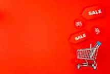 Shopping cart with sale tags on vibrant red backdrop promoting discounts. (Foto: https://kaboompics.com/ / Pexels)